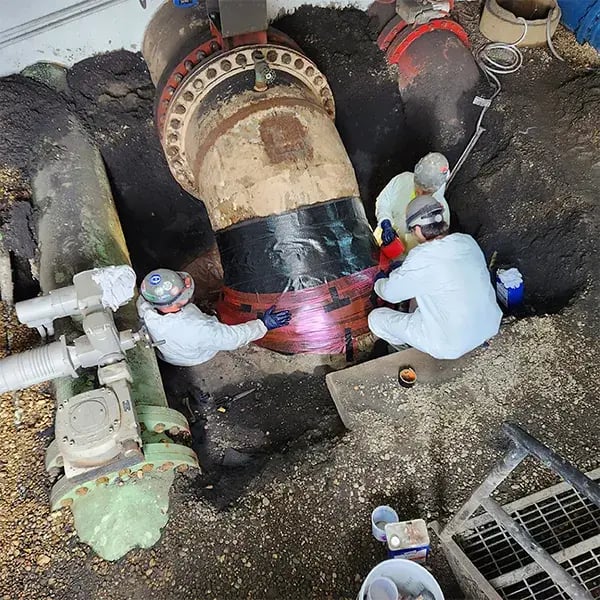 workers apply belzona superwrap composite repair material for soil line pipe corrosion repair